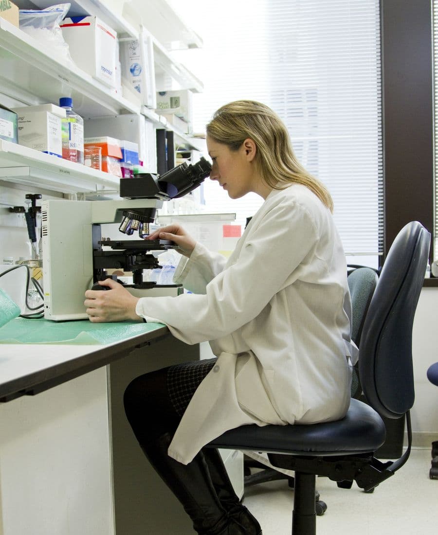 Scientist in a white lab coat looking into a microscope in a bright laboratory