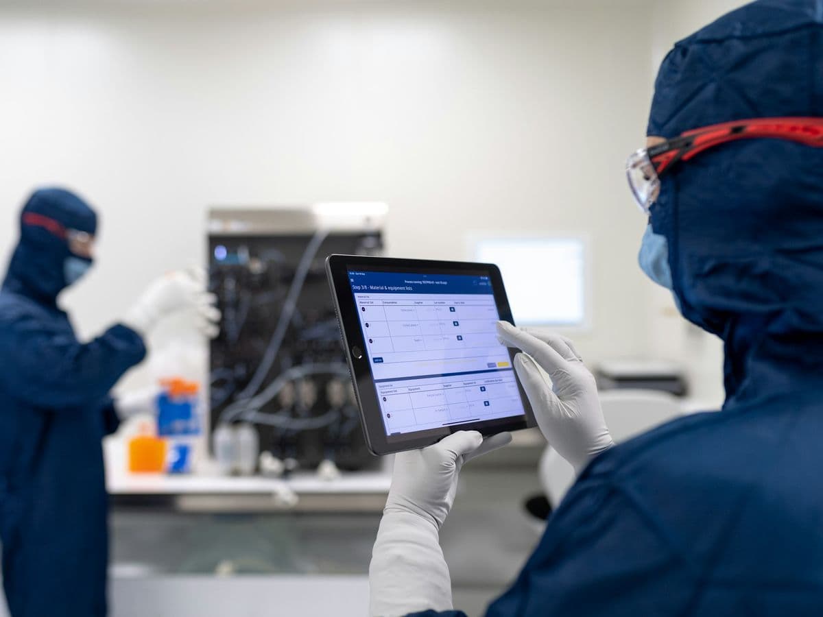Technician in cleanroom gear using a tablet beside laboratory equipment